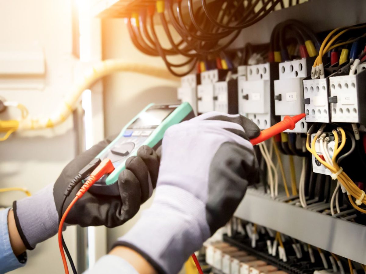 Electrical engineer using digital multi-meter measuring equipment to checking electric current voltage at circuit breaker and cable wiring system in main power distribution board.